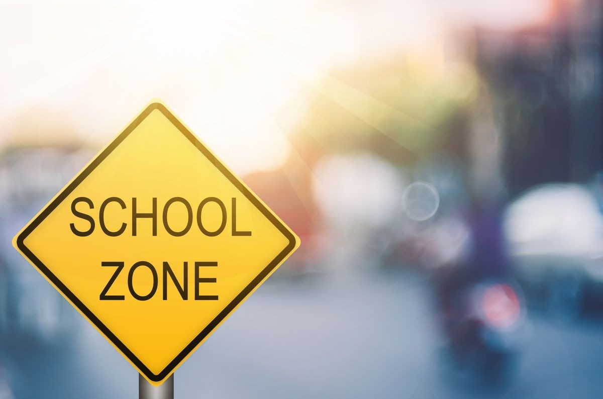 School zone warning sign on blur traffic road with colorful bokeh light abstract background. Copy space of transportation and travel concept. Vintage tone filter color style.